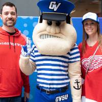 Two alumni pose with Louie while doing the Laker hand gesture at the Detroit Red Wings GVSU Night